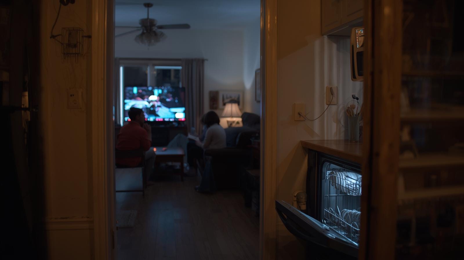 Família assistindo TV à noite enquanto lava-louças opera silenciosamente na cozinha, simbolizando rotina mais leve e presente.